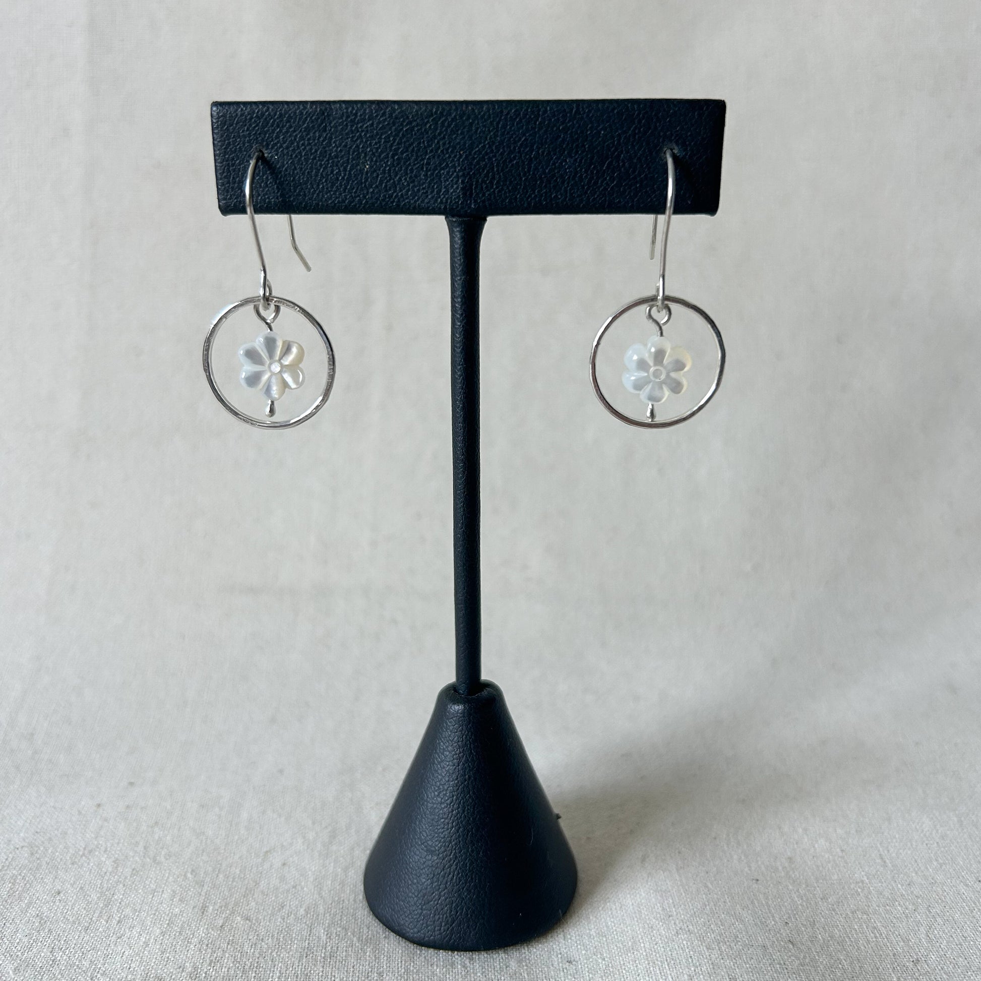 White flower earrings dangling from black display stand with gray background 