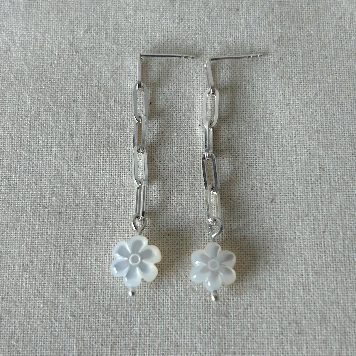 White flower earrings with silver chain laying on a gray background 