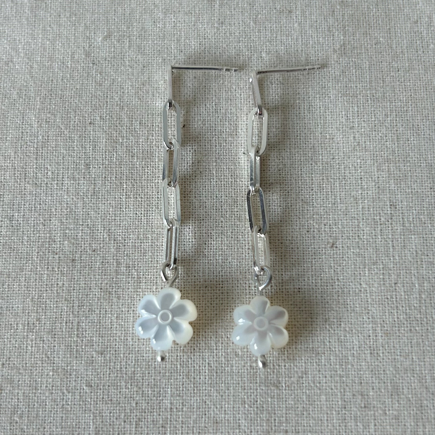 White flower earrings with silver chain laying on a gray background 