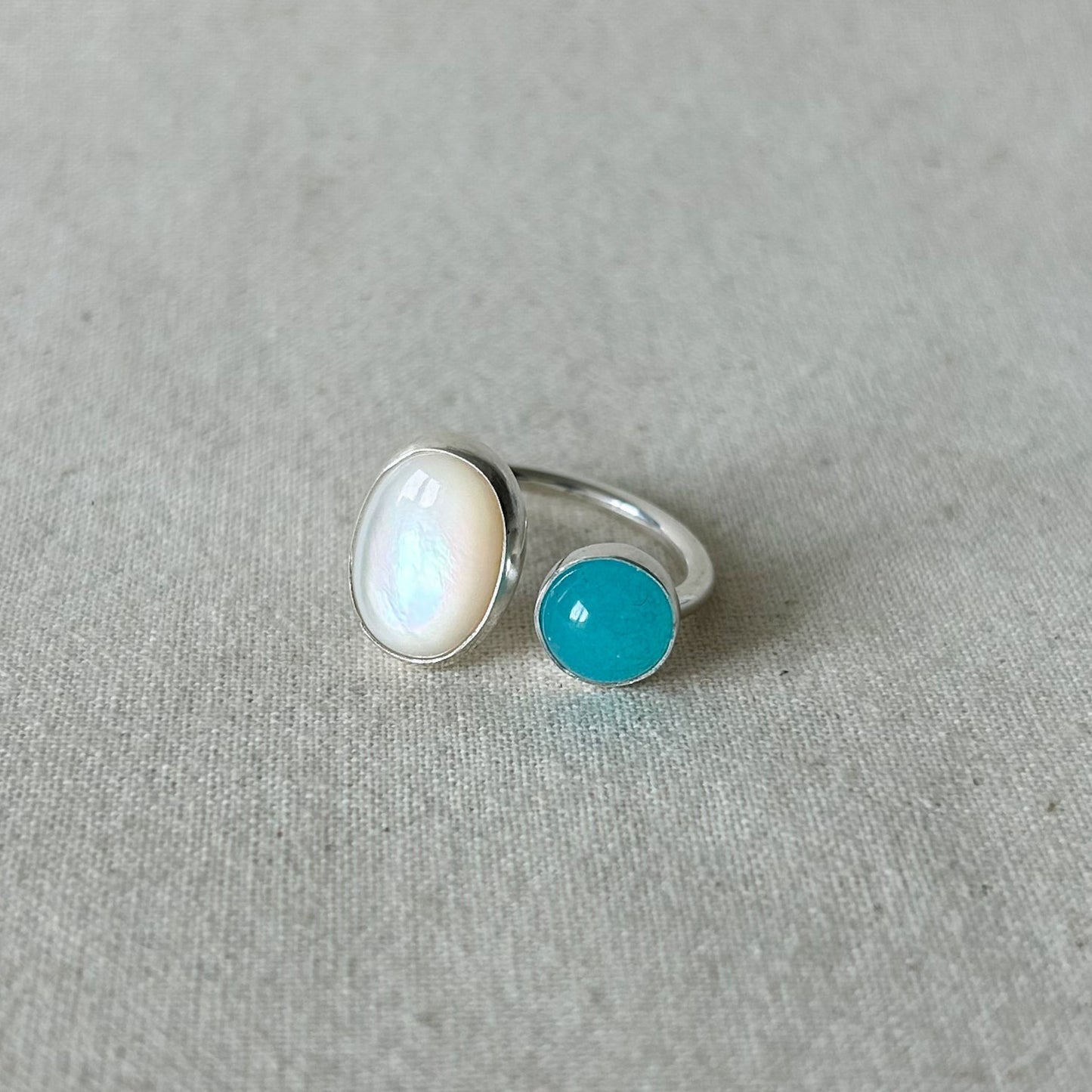 White oval stone ring with smaller blue stone on a gray background 