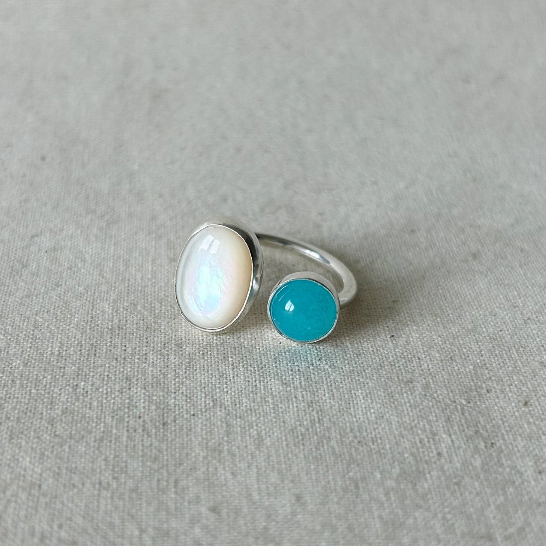 White oval stone ring with smaller blue stone on a gray background 