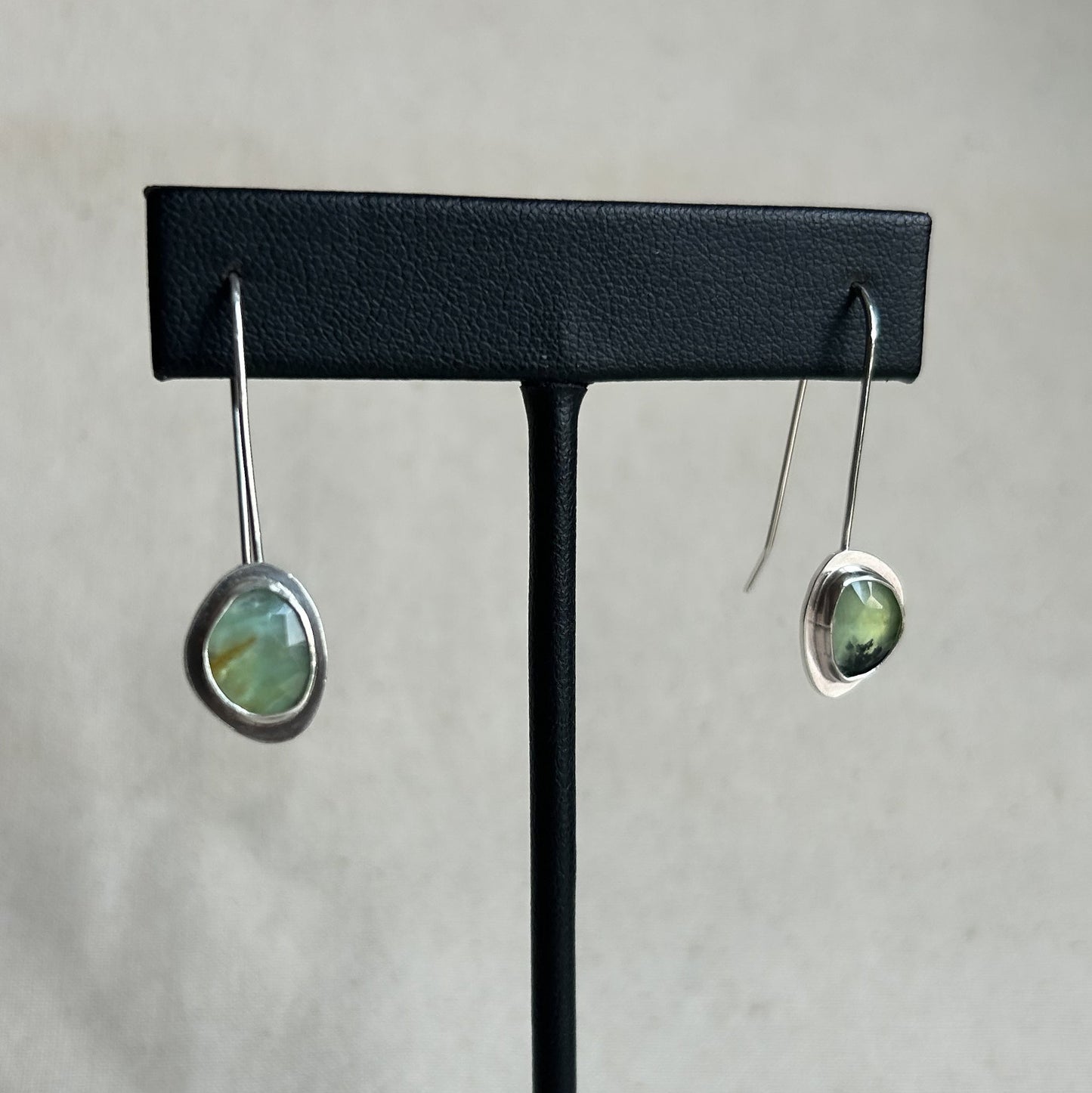 Pair of earrings on a black earring stand against a light gray background