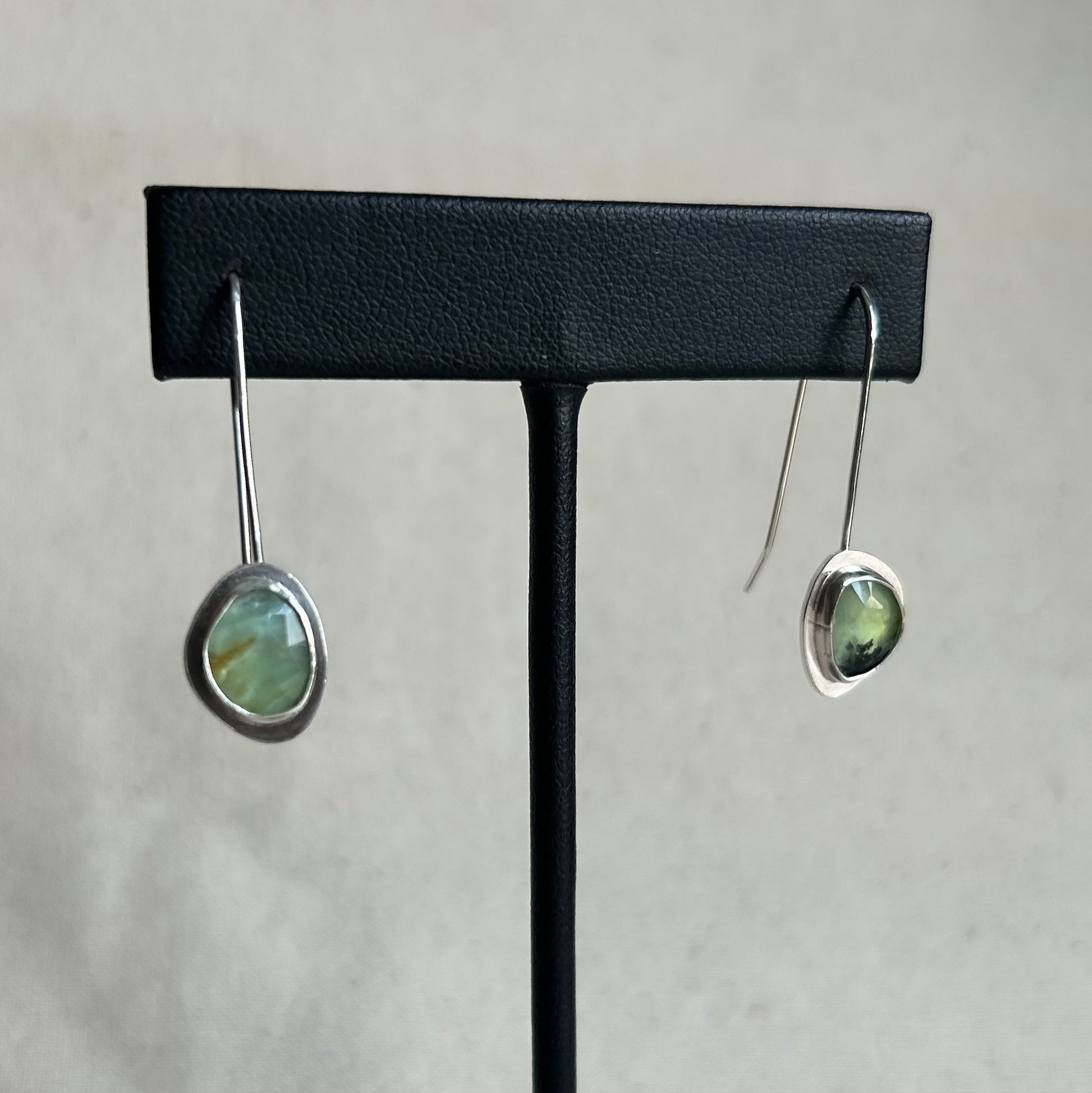 Pair of earrings on a black earring stand against a light gray background