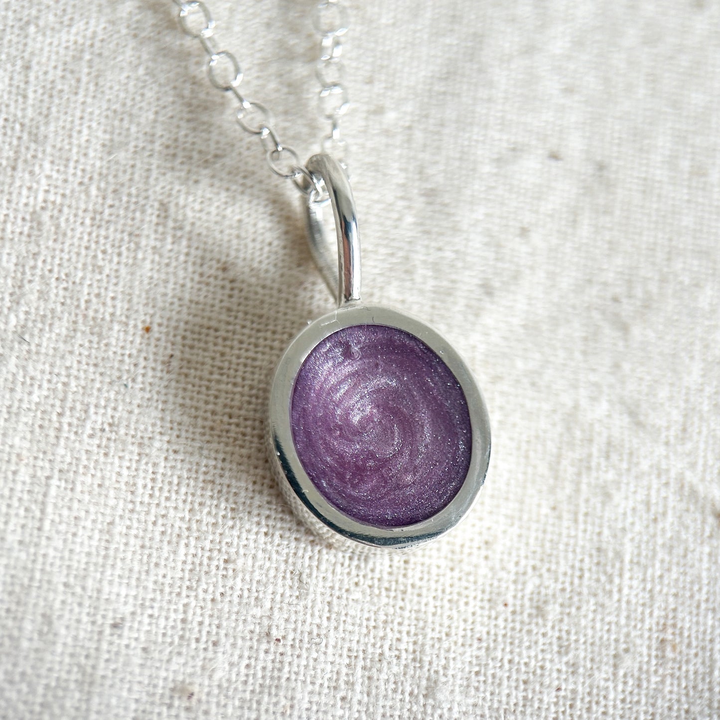 Purple ashes pendant on a silver chain against a beige fabric background