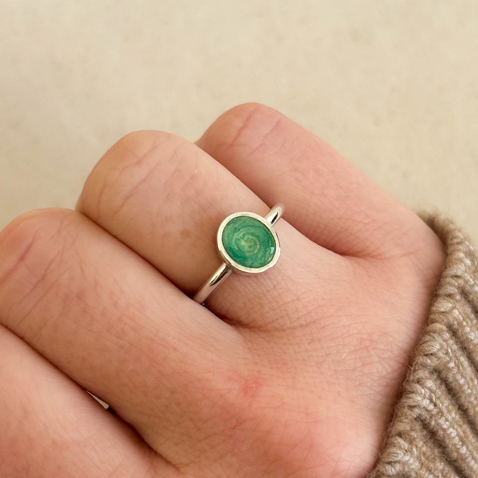Silver ring with a green gemstone on a finger against a beige background