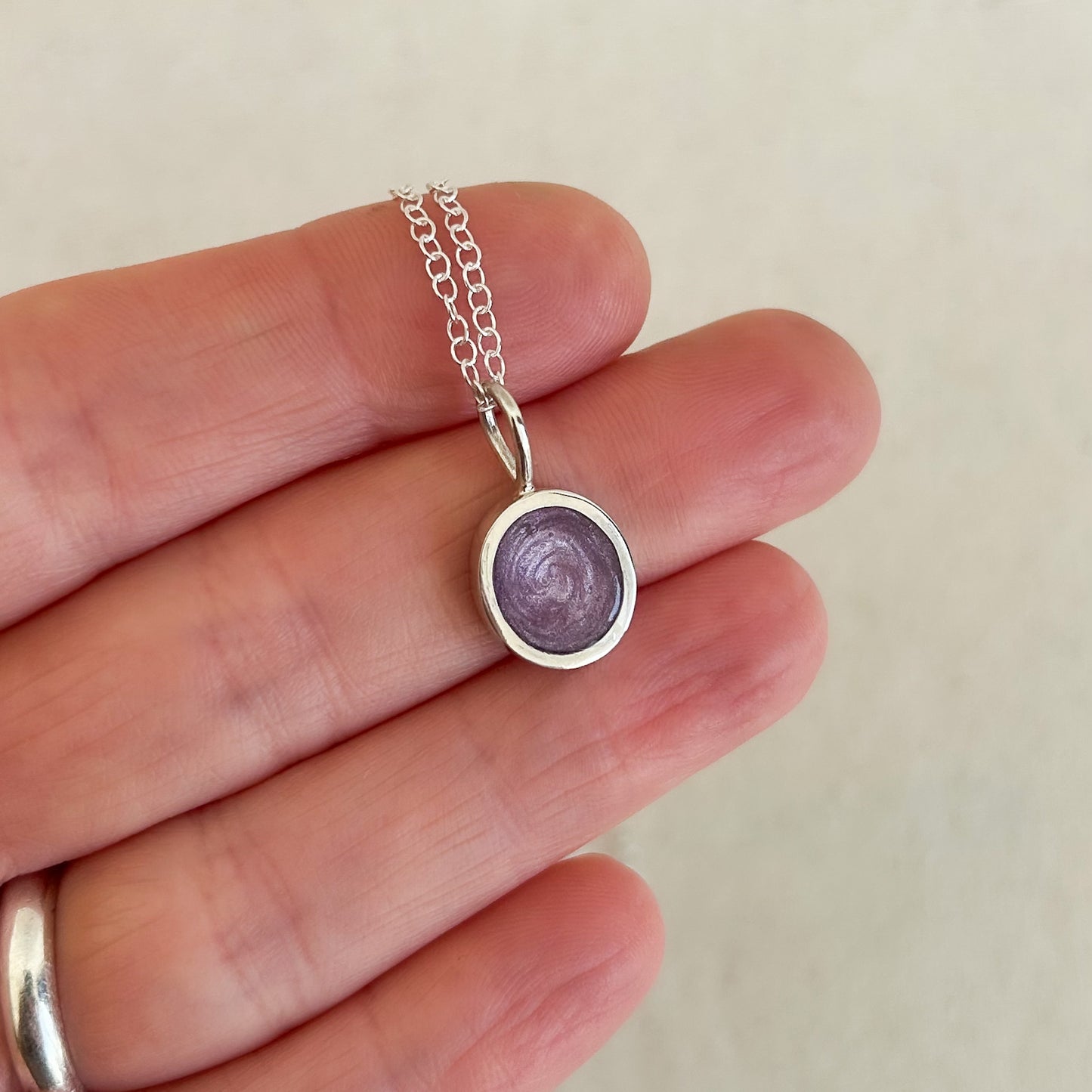 Small silver pendant with a purple stone held between fingers on a light background