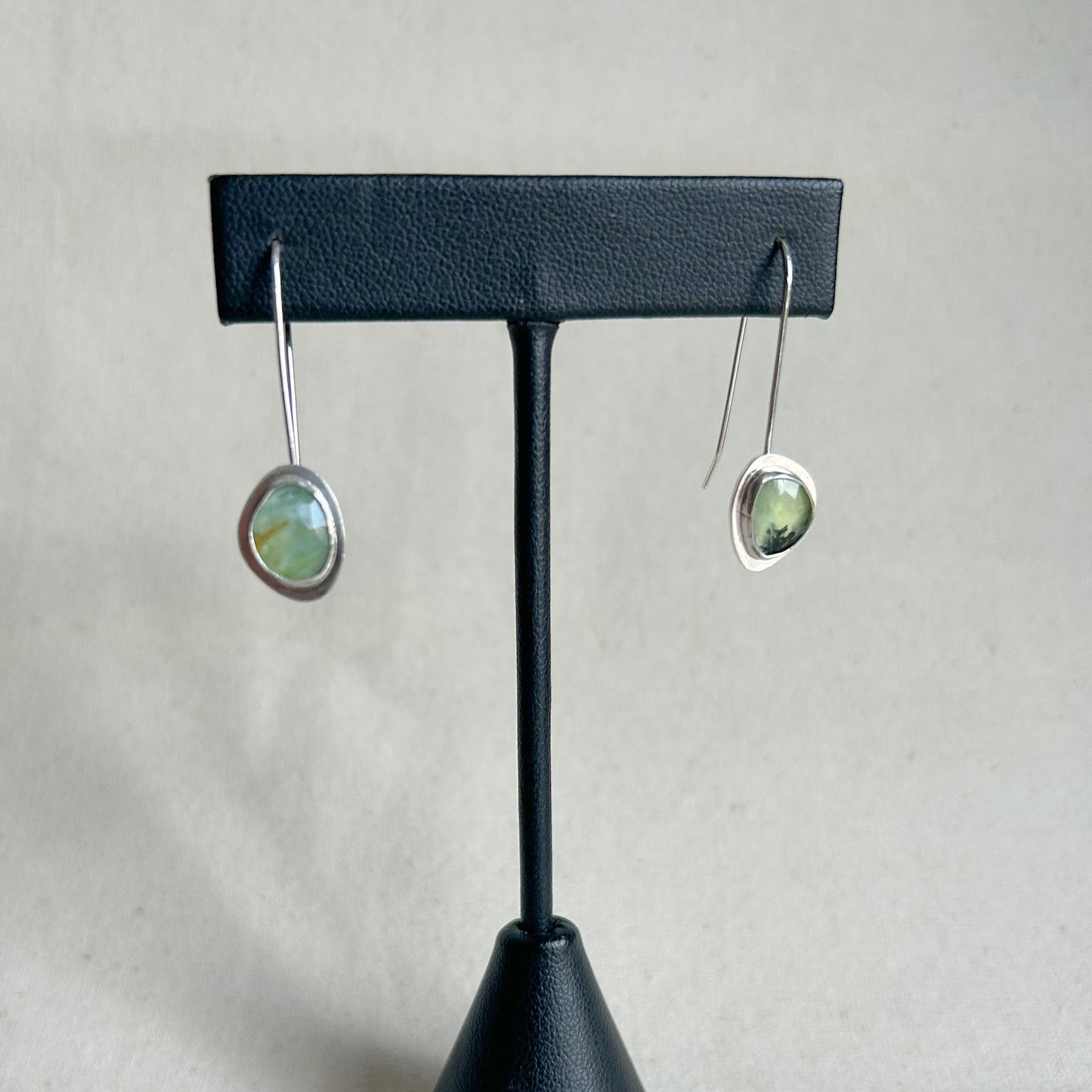 Pair of earrings on a black earring stand against a gray background