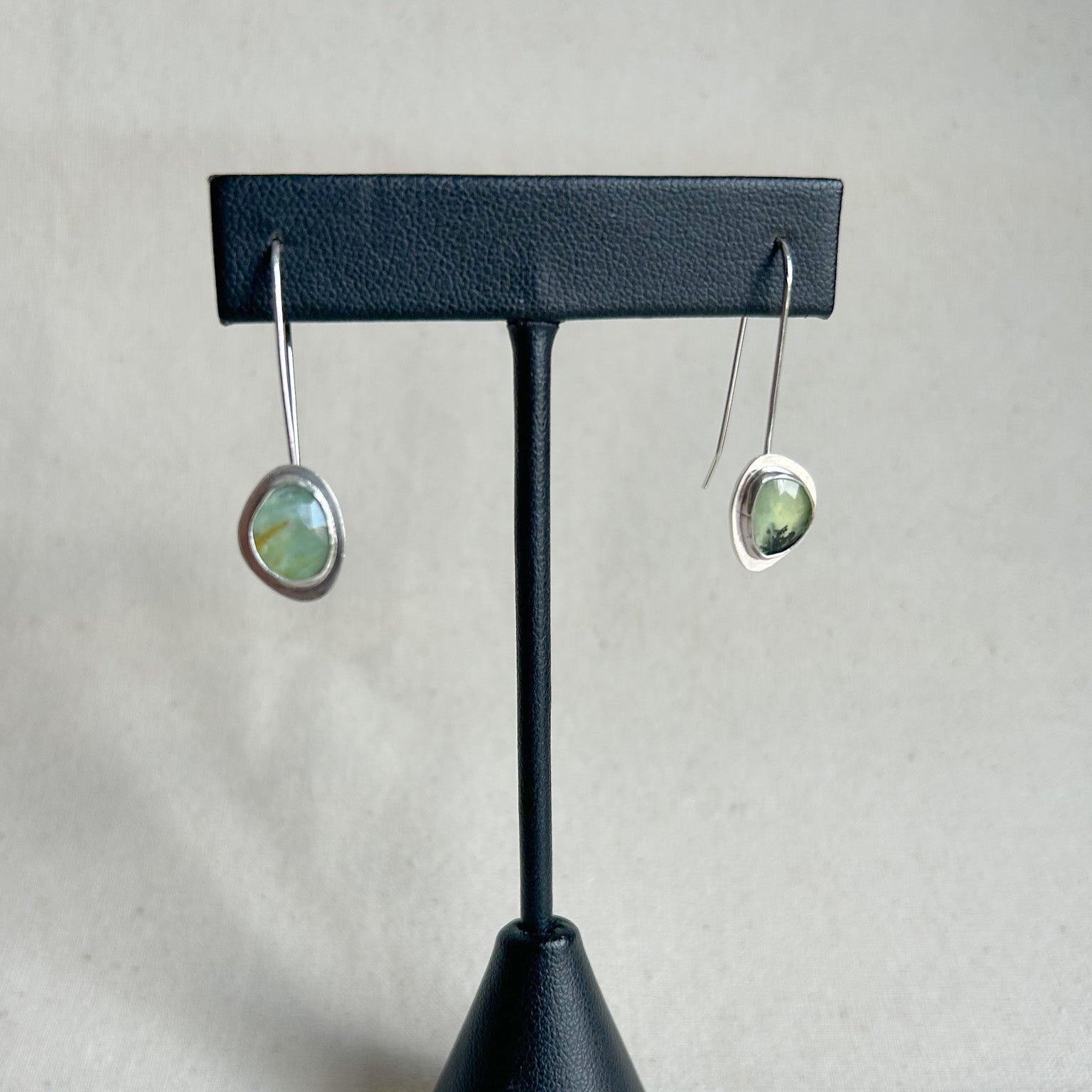 Pair of earrings on a black earring stand against a gray background