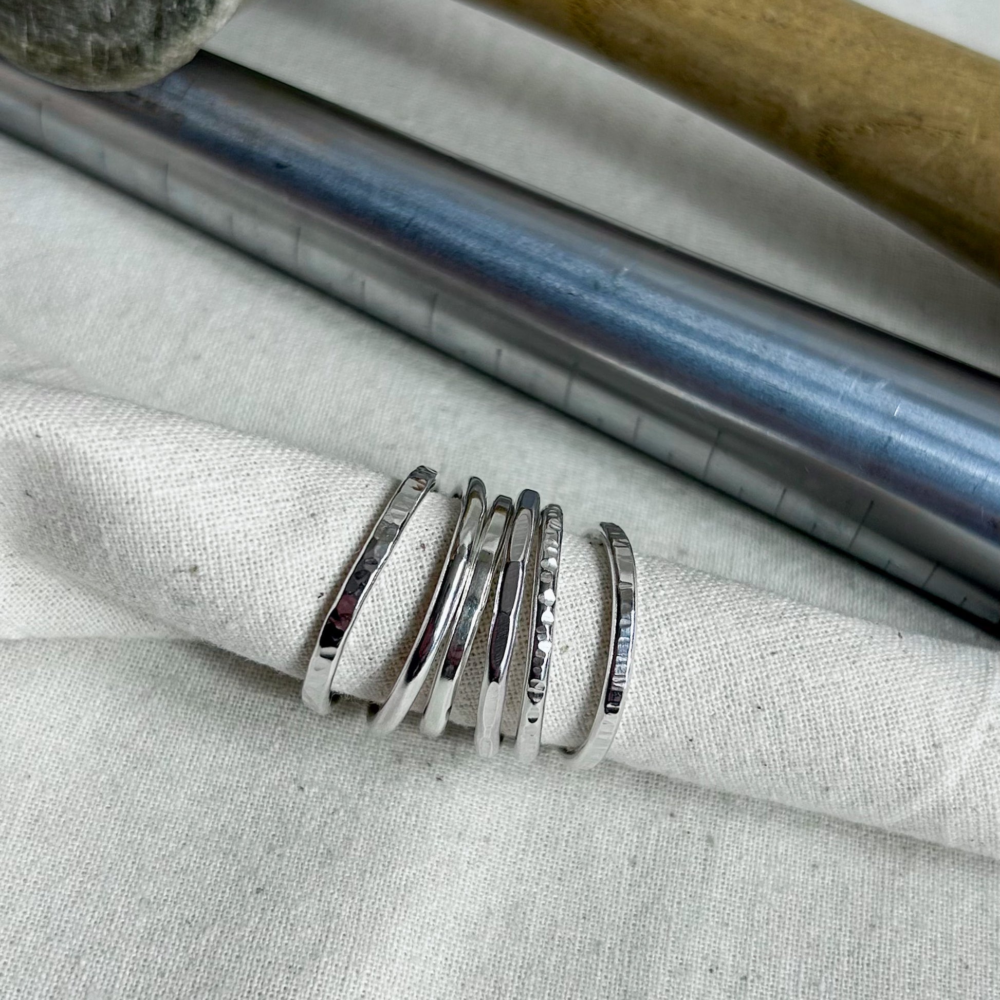 A set of five polished silver rings with varying textured finishes, displayed on a folded light beige linen cloth.