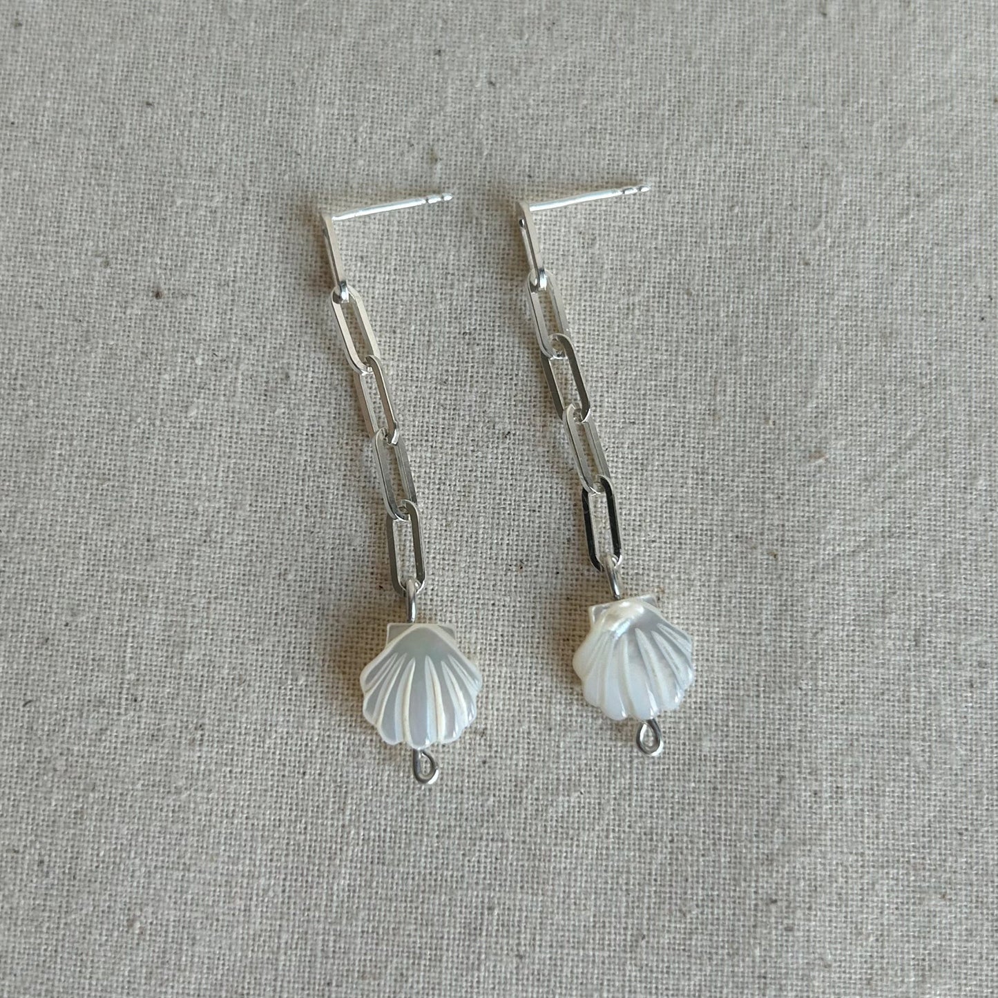 White shells on a silver chain earring on grey background 