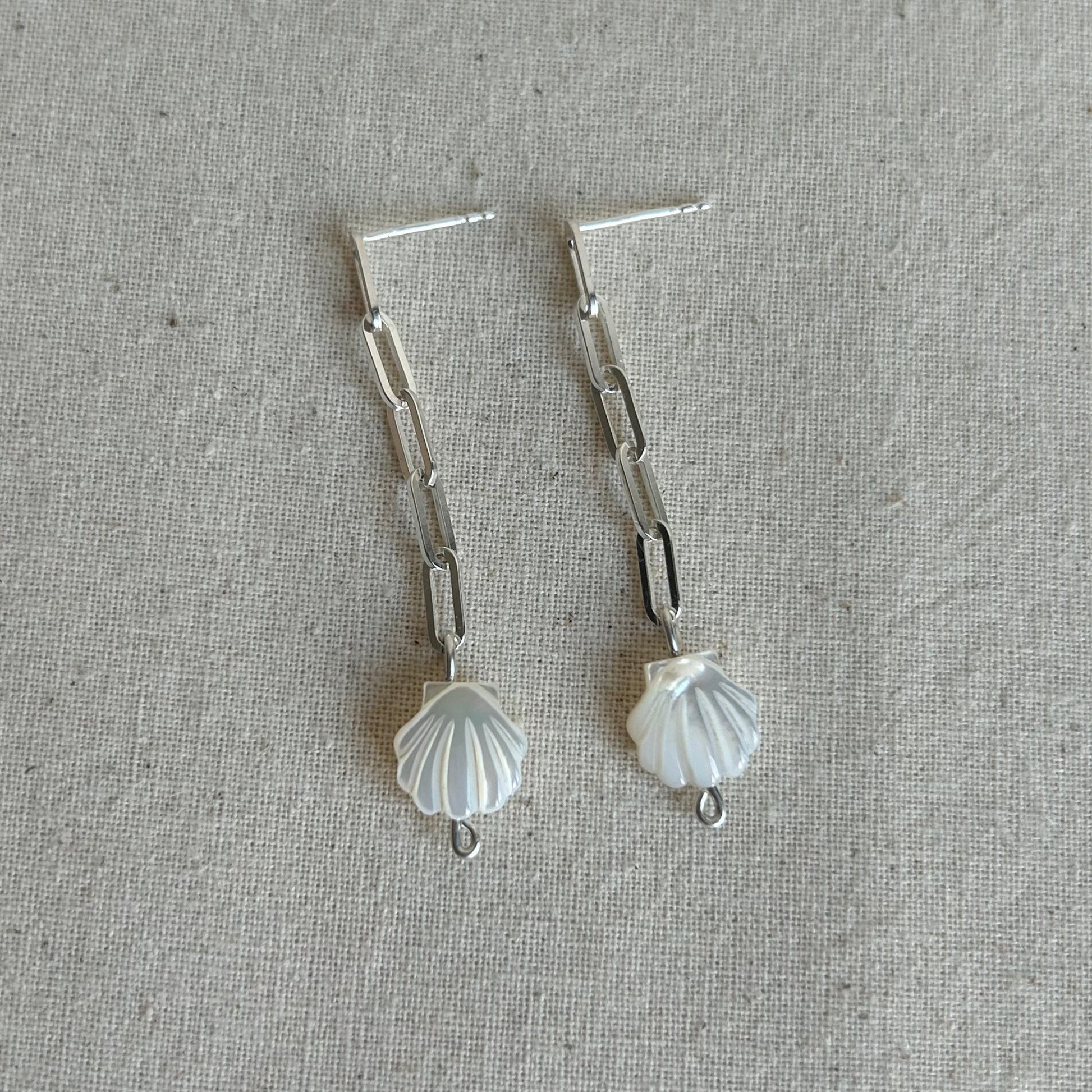 White shells on a silver chain earring on grey background 
