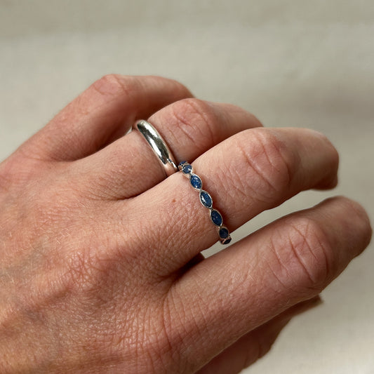 Hand wearing two rings, one silver and one with blue stones, on a neutral background