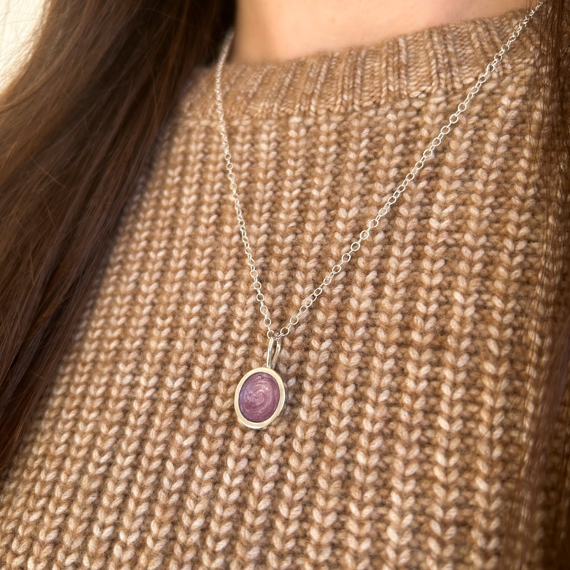 Necklace with a purple pendant on a person wearing a brown knitted sweater