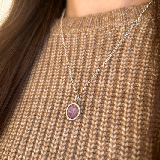 Necklace with a purple pendant on a person wearing a brown knitted sweater