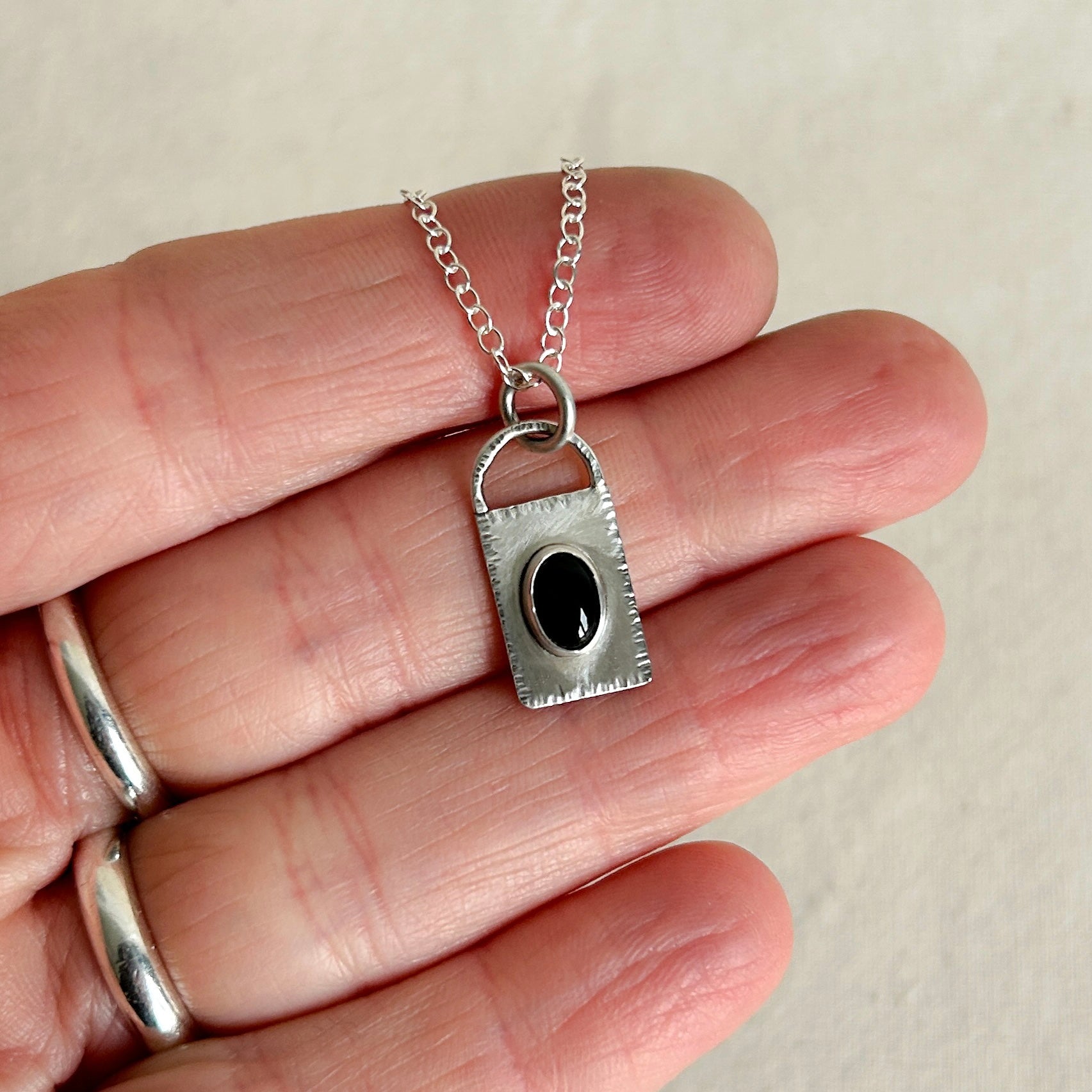 Silver pendant with a black stone held between fingers on a neutral background