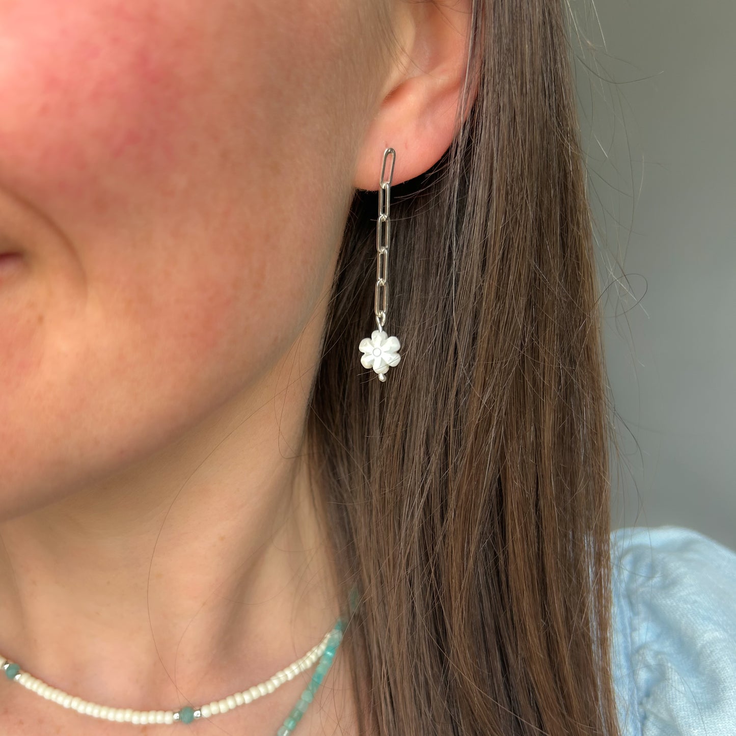 Person wearing silver chain dangle earrings with white flower at the bottom