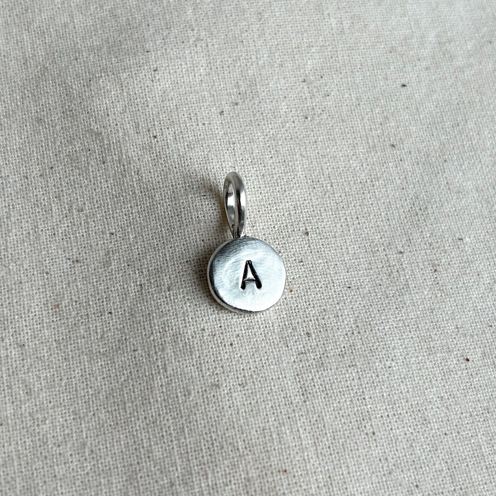 Silver pendant with letter 'A' on a beige fabric background