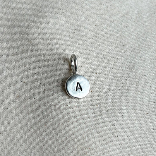 Silver pendant with letter 'A' on a beige fabric background