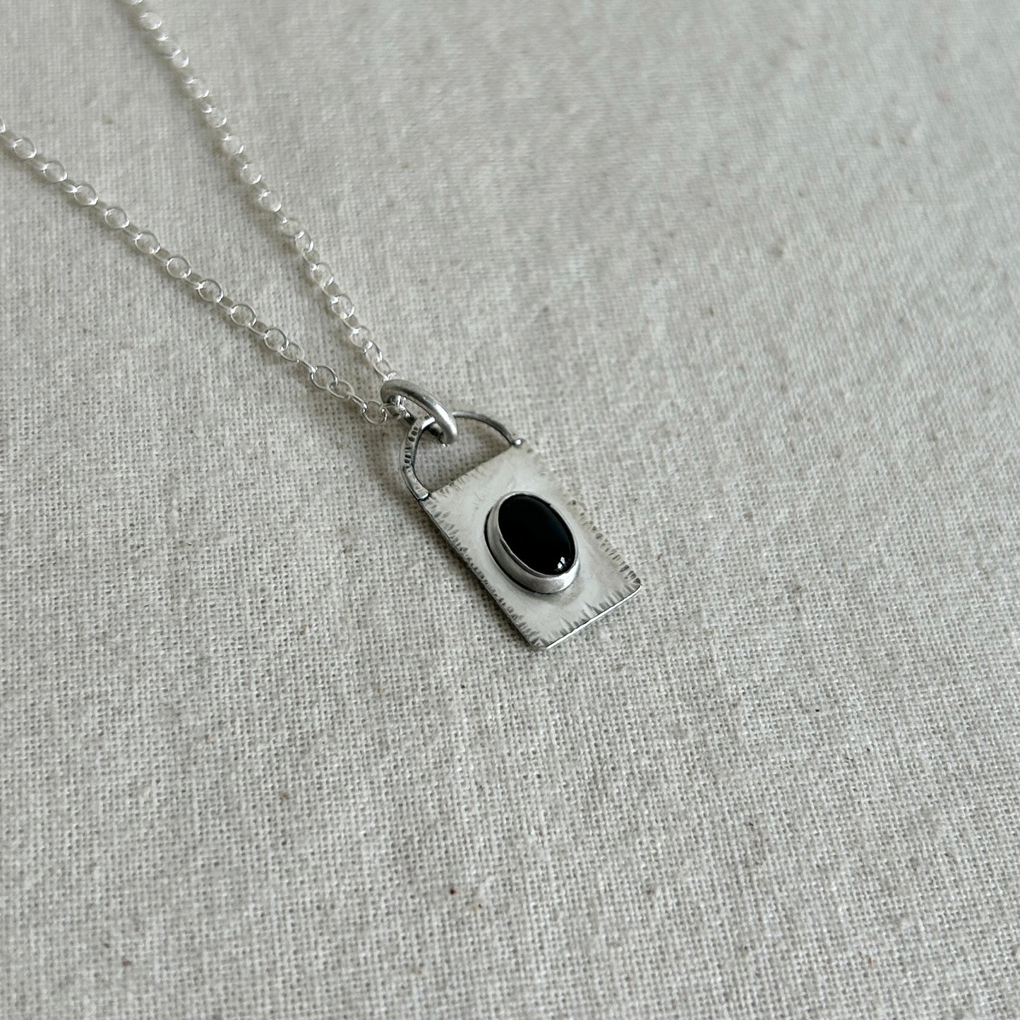 Silver necklace with a pendant featuring a black gemstone on a gray fabric background