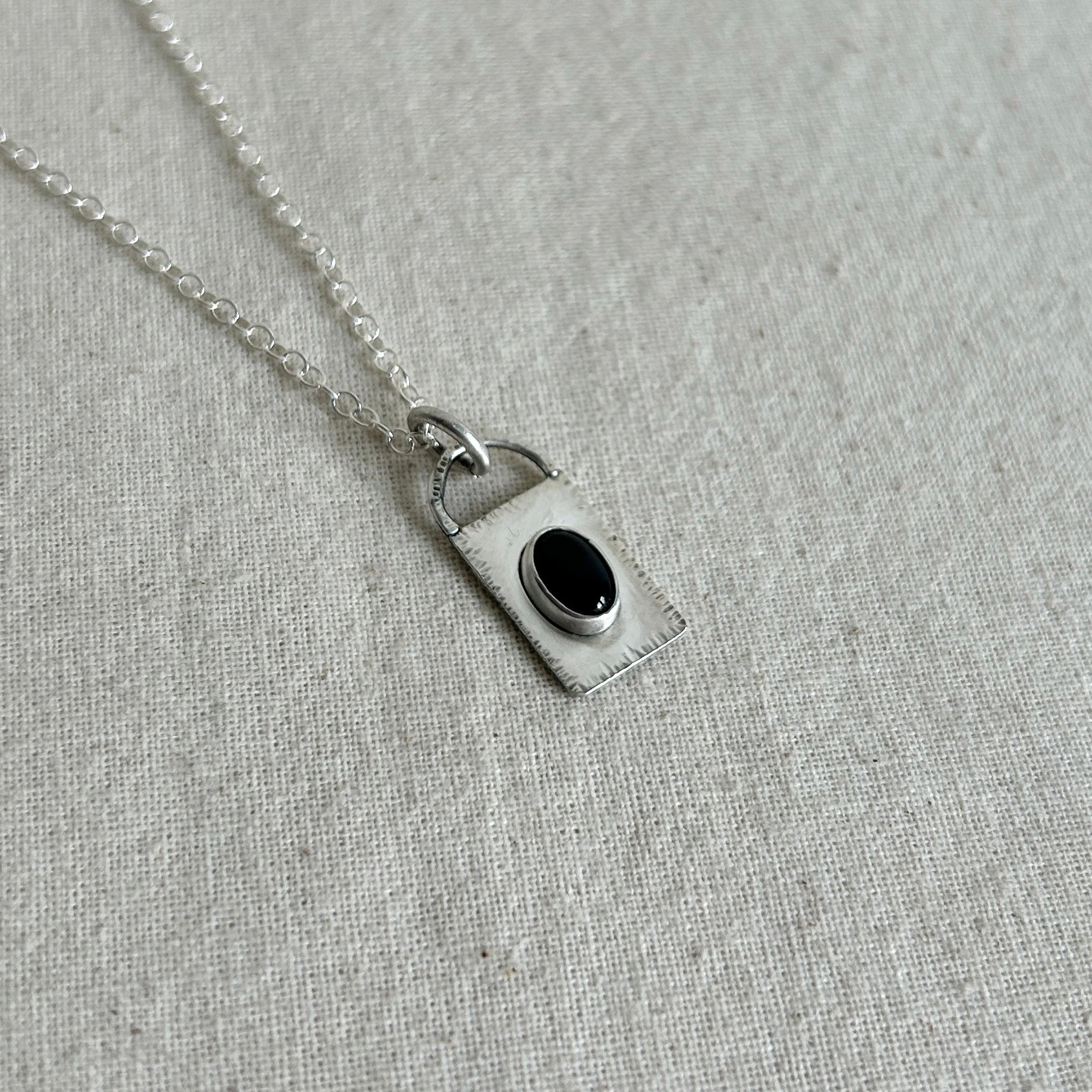 Silver necklace with a pendant featuring a black gemstone on a gray fabric background