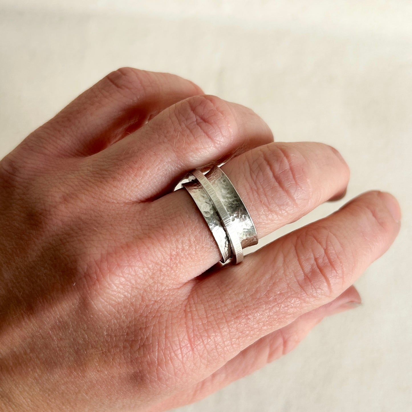 Silver spinner ring on models hand with grey background 