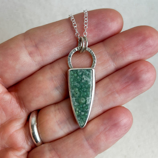 Silver pendant with green gemstone held in hand