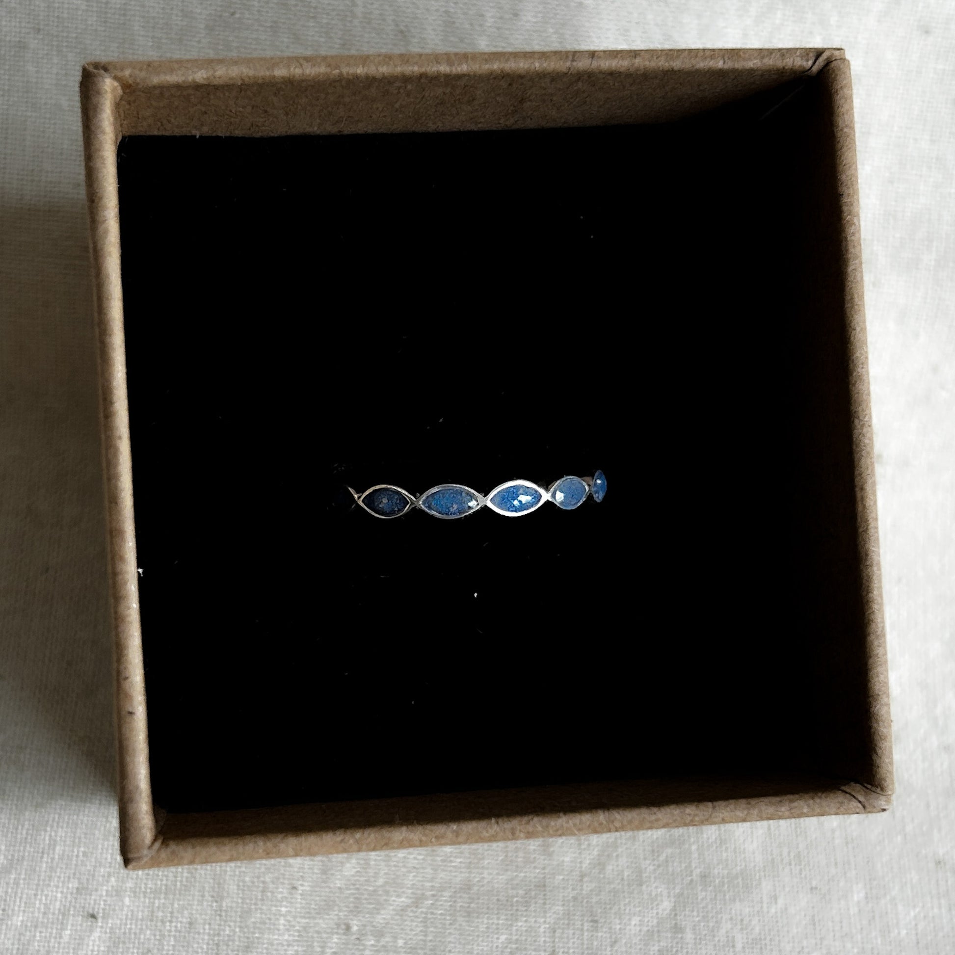 Silver ring with blue stones in a brown box on a textured surface