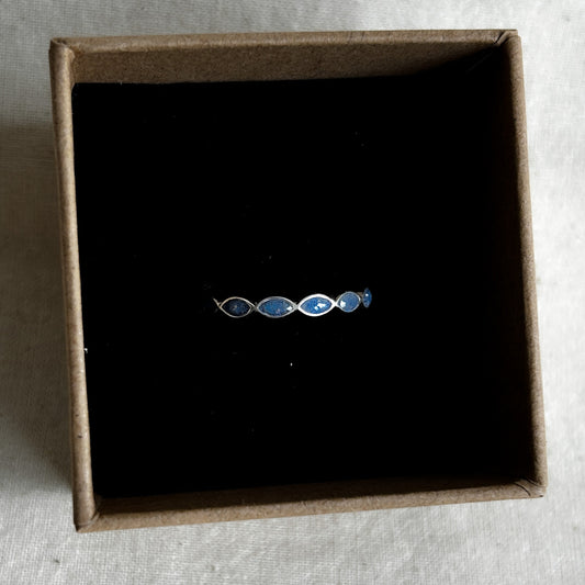 Silver ring with blue stones in a brown box on a textured surface