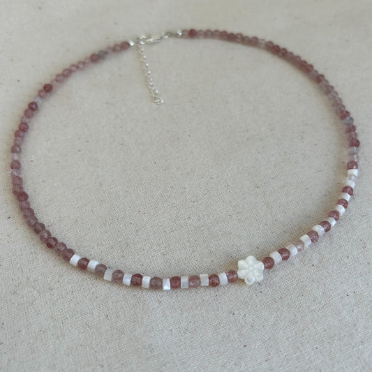 Beaded necklace with a white flower pendant on a beige background