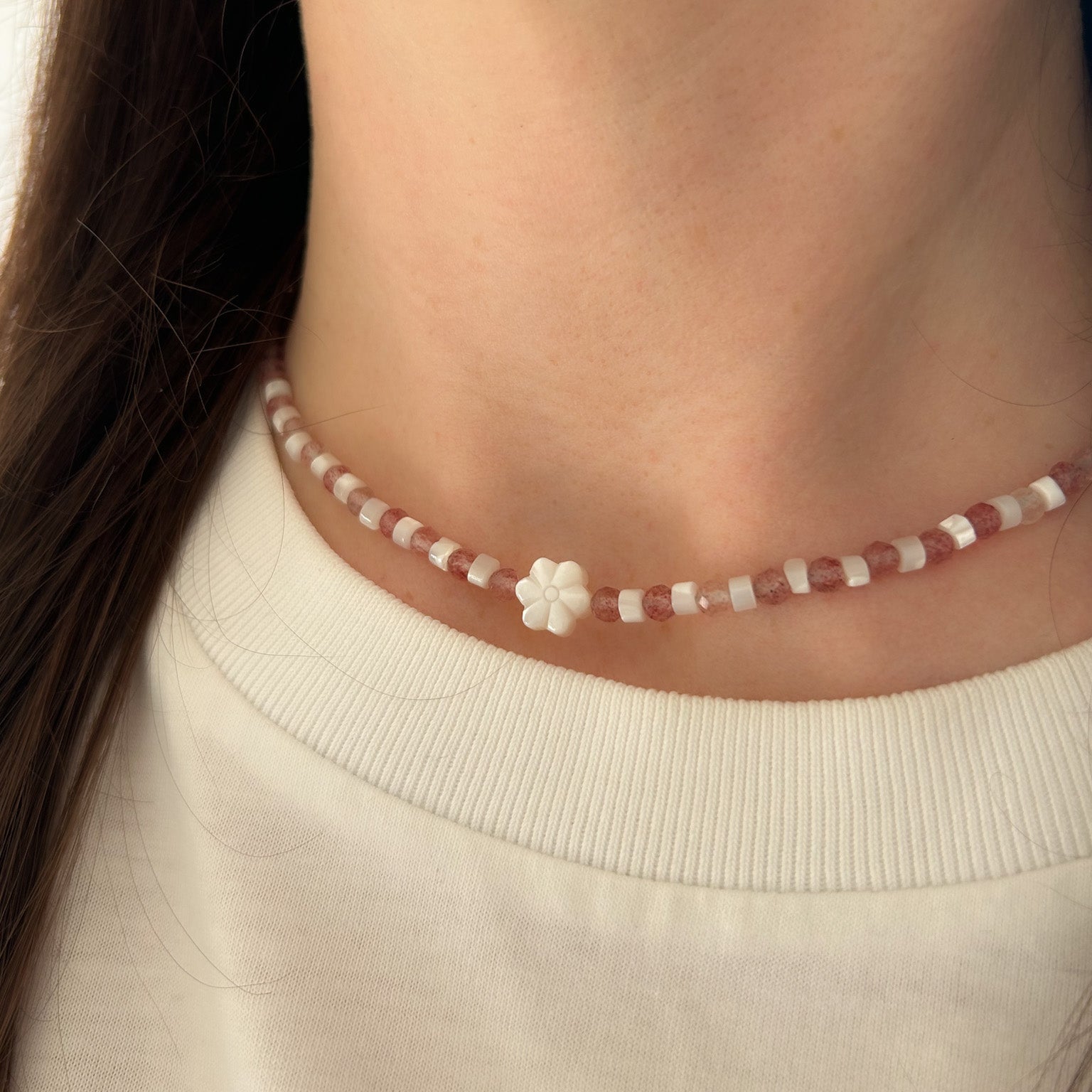 Close-up of a person wearing a delicate necklace with a flower pendant on a neutral background