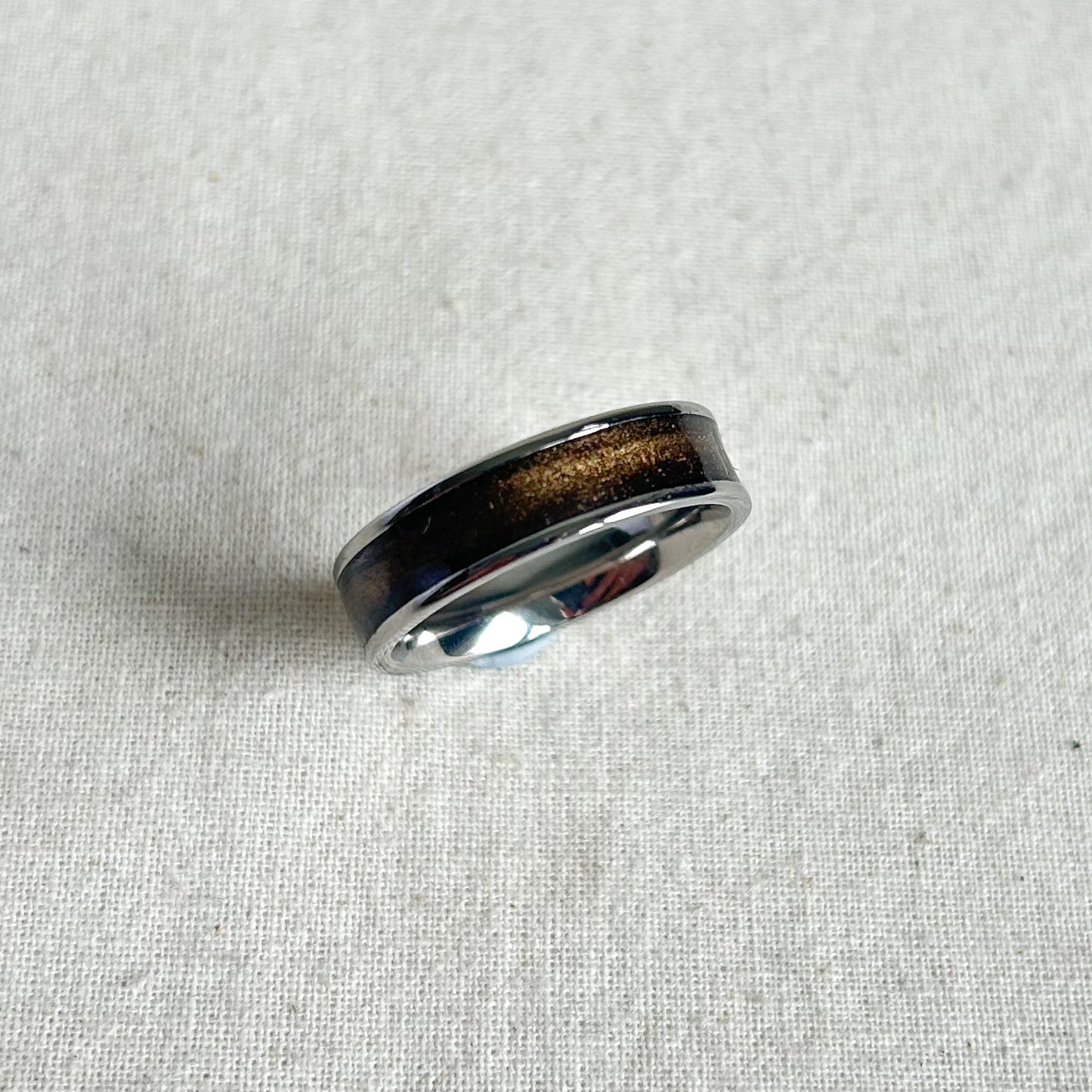 Silver ring with a dark brown inlay on a light gray fabric background