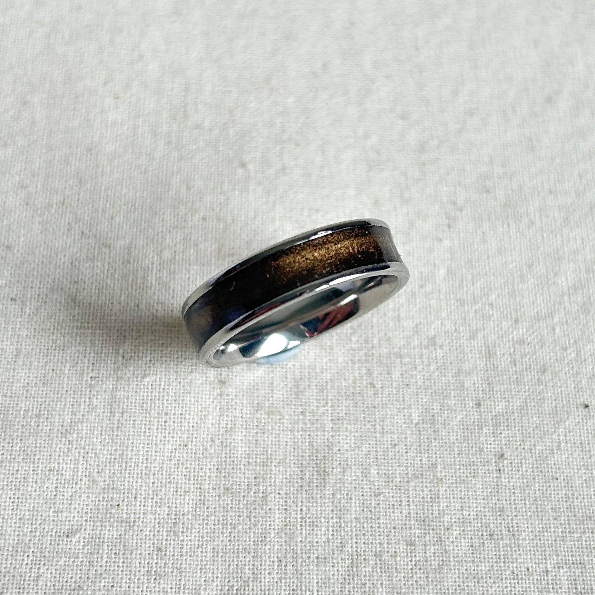 Silver ring with a dark brown inlay on a light gray fabric background