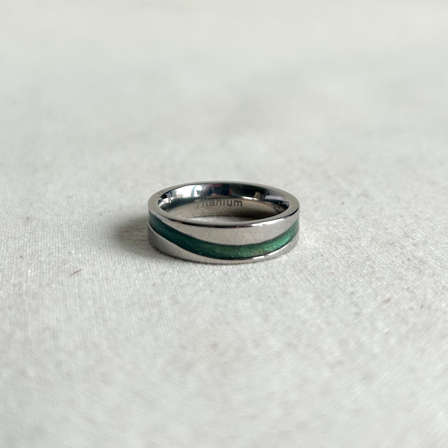 Silver ring with a green inlay on a light gray background