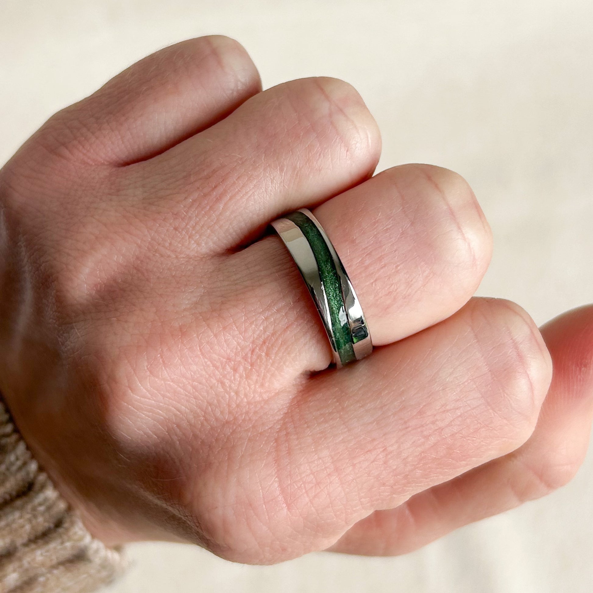 Hand wearing a silver ring with green inlay on a neutral background