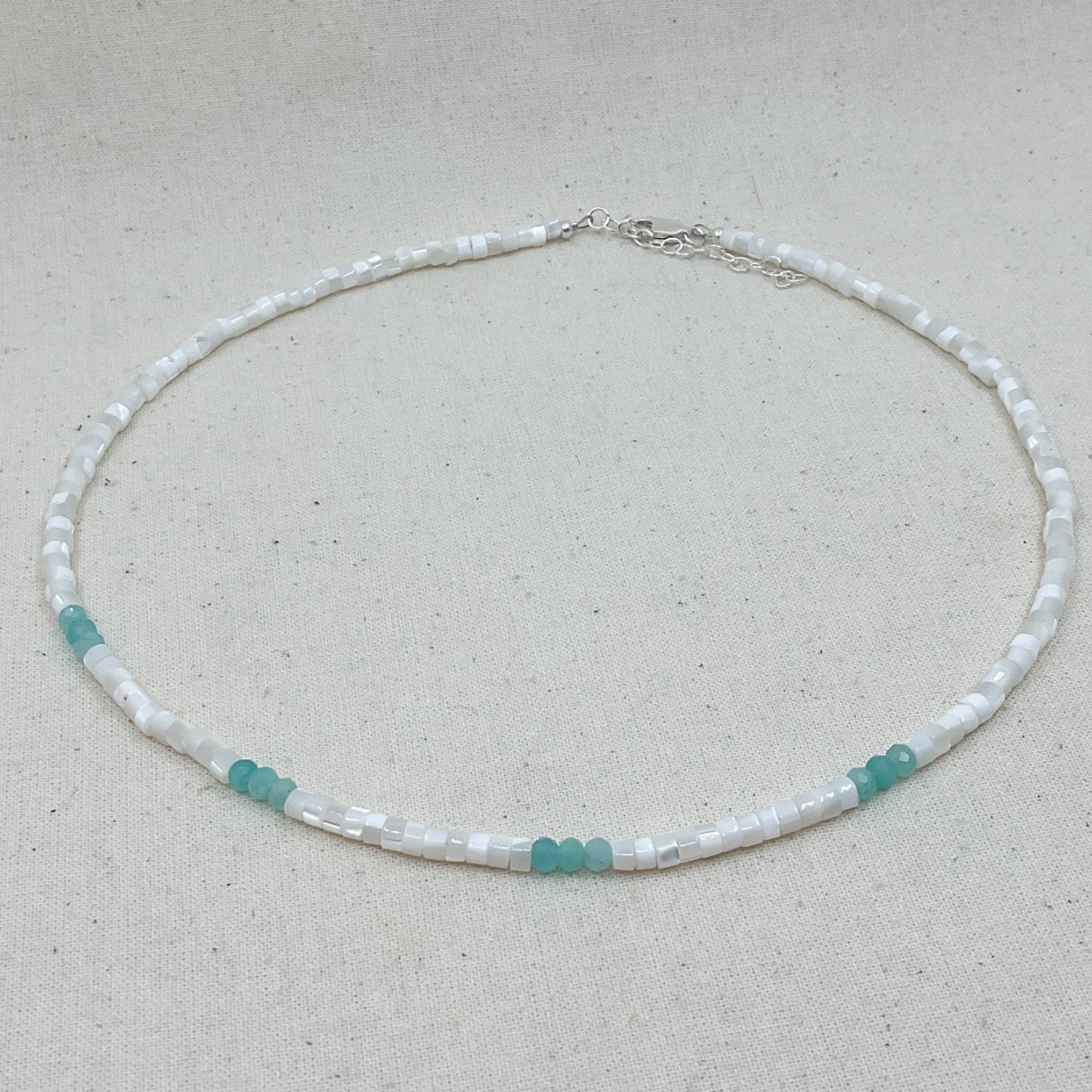 Necklace with white and turquoise beads on a light gray background