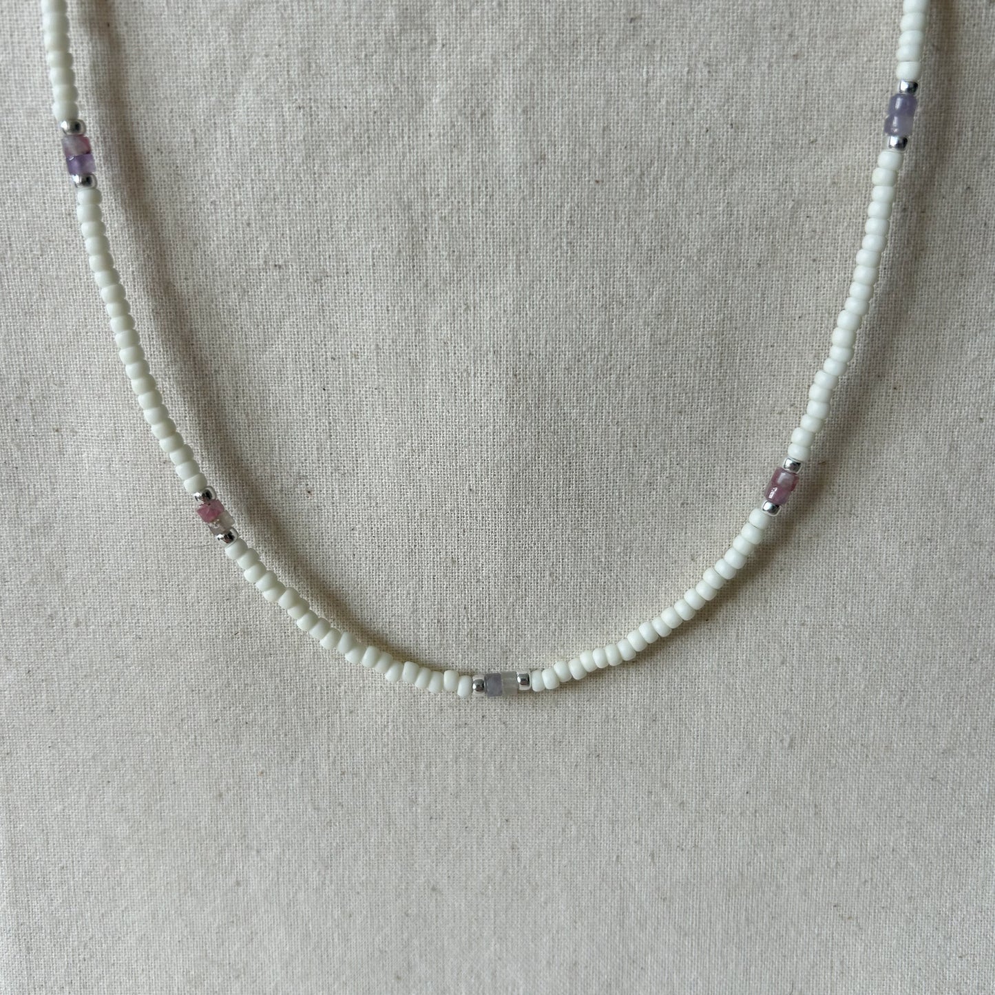 White beaded necklace with pink beads on a gray background 