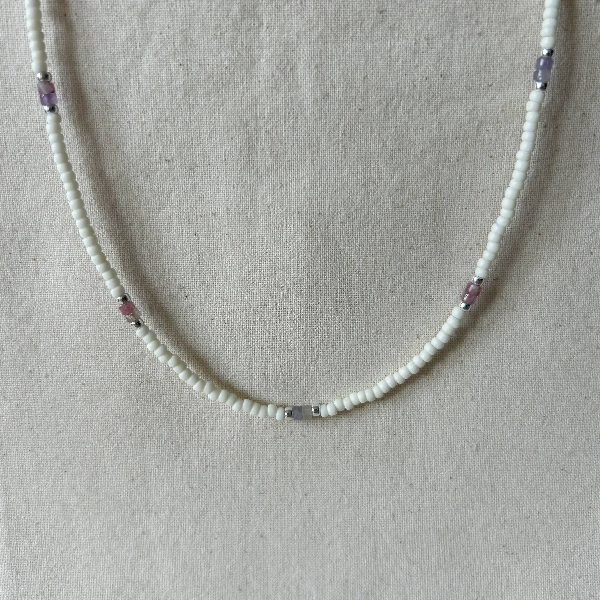 White beaded necklace with pink beads on a gray background 