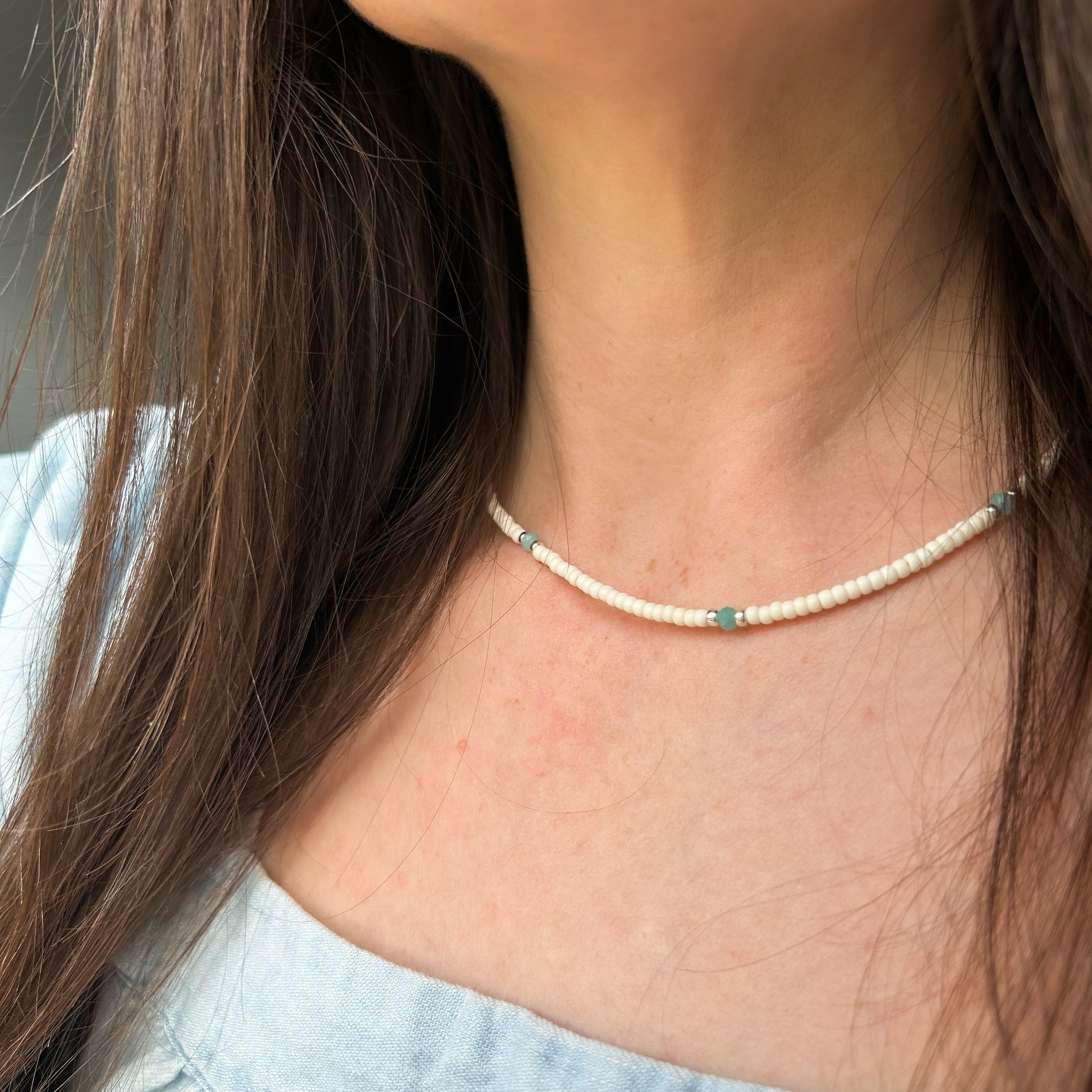 White beaded necklace shown on model wearing blue shirt