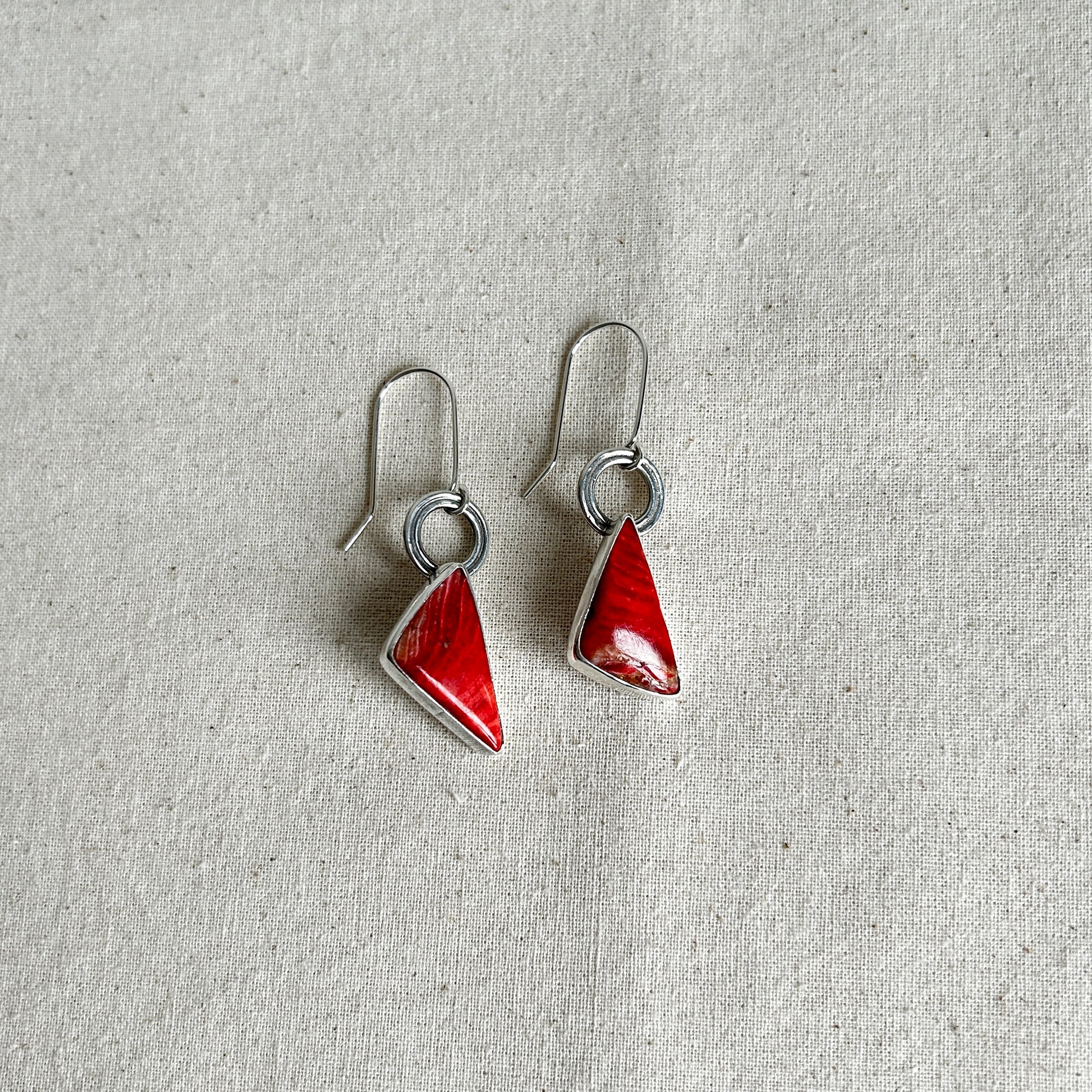 A pair of silver dangle earrings with red Mookaite Jasper stones set in them. 